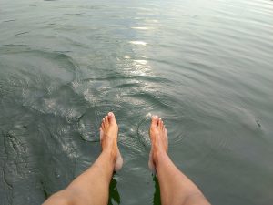 Bare feet dangling into the still, clear waters of Begnas Lake with ripples spreading gently around them. 