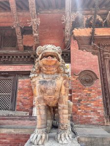 A large stone lion guardian statue with open jaws and ornate carvings guarding the entrance of a Hindu temple in Patan, Nepal. 
