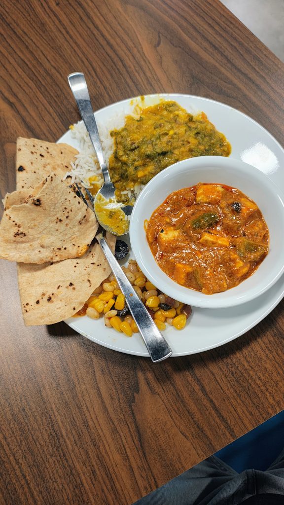 A plate with naan, yellow lentil curry over rice, a bowl of paneer curry, and corn salad with black beans.
