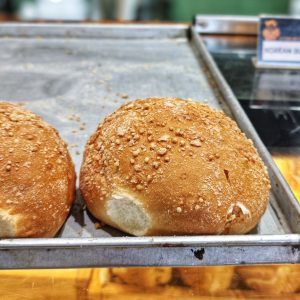 Freshly baked golden bread rolls with a crunchy crumb-dusted crust resting on a bakery tray 