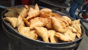 A tray filled with crispy, golden-brown samosas, basking in sunlight. 
