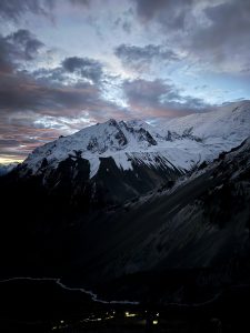 Dawn ignites the sky over snow-clad peaks, casting the valley below in velvety shadows. Along the Tilicho trail, a faint glacial river cuts through the darkness. At the mountain’s base, a line of trekkers embarks on an alpine start, their headlamps piercing the void like fireflies against the Himalayas. 
