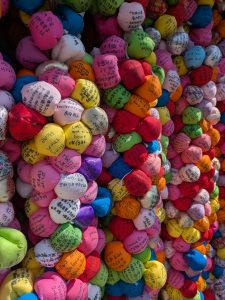 Colorful fabric prayer balls covered with handwritten wishes and messages at Yasaka Koshindo Temple in Kyoto, Japan. The vibrant kukurizaru charms, inspired by a traditional Japanese folk belief, create a striking display symbolizing hopes, gratitude, personal aspirations, and spiritual devotion.