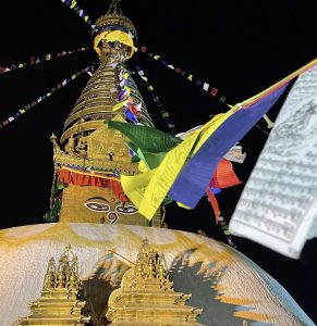
Golden stupa with Buddha eyes at night, adorned with vibrant prayer flags. The scene conveys peace and spirituality against a dark sky.