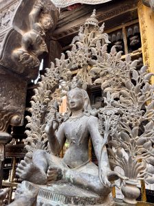 A serene bronze Tara or Lakshmi goddess statue seated in meditation posture with an elaborate floral aureole, inside a richly decorated Newari temple interior, Kathmandu, Nepal. 