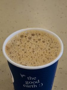A freshly brewed cup of hot coffee topped with a rich layer of froth, served in a takeaway cup. The warm tones and detailed bubbles create a cozy and inviting feel, perfect for a refreshing coffee break. Captured in Palazhi, Kozhikode, Kerala. 