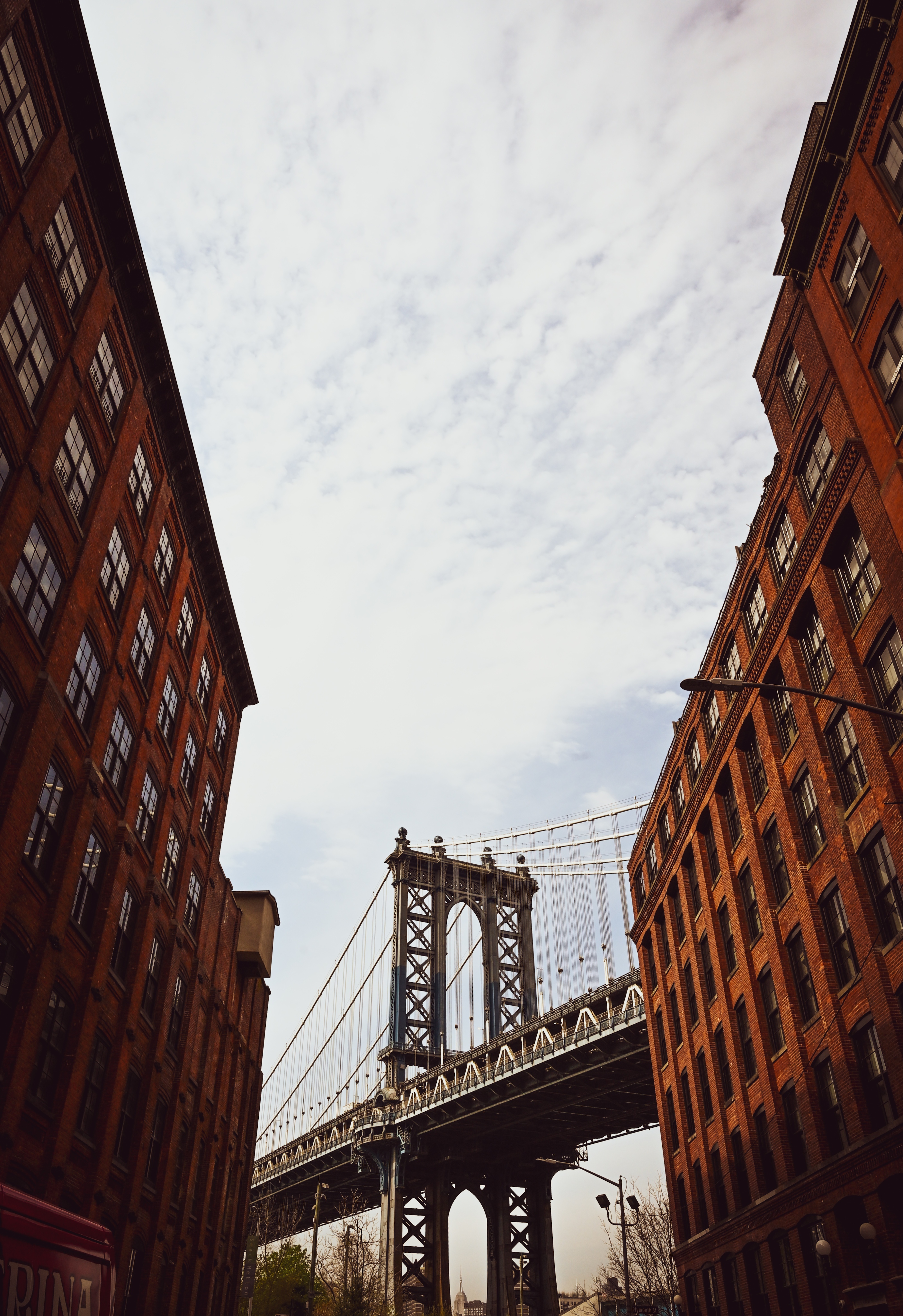 Manhattan Bridge tower piercing through a narrow canyon of historic red brick warehouses