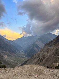Dramatic mountain valley with winding river, rugged peaks, and towering clouds illuminated by evening light. 