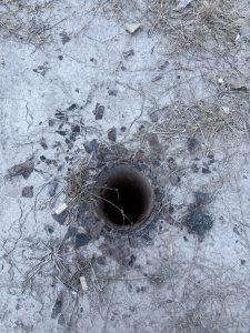 A rusted pole beside cracked concrete, dry grass, and scattered debris.