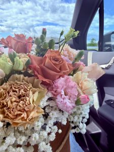 A vibrant bouquet of roses, carnations, and baby's breath in a car interior, set against a bright blue sky with scattered clouds