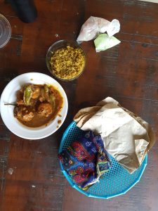 A table with a bowl of traditional Pakistani daal, served with yellow rice, flatbreads wrapped in colorful cloth, and a side of peppers.
