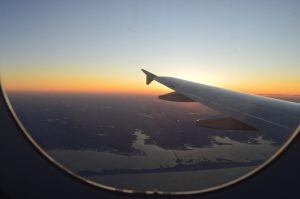 View from an airplane window showing the wing above a landscape at sunset.