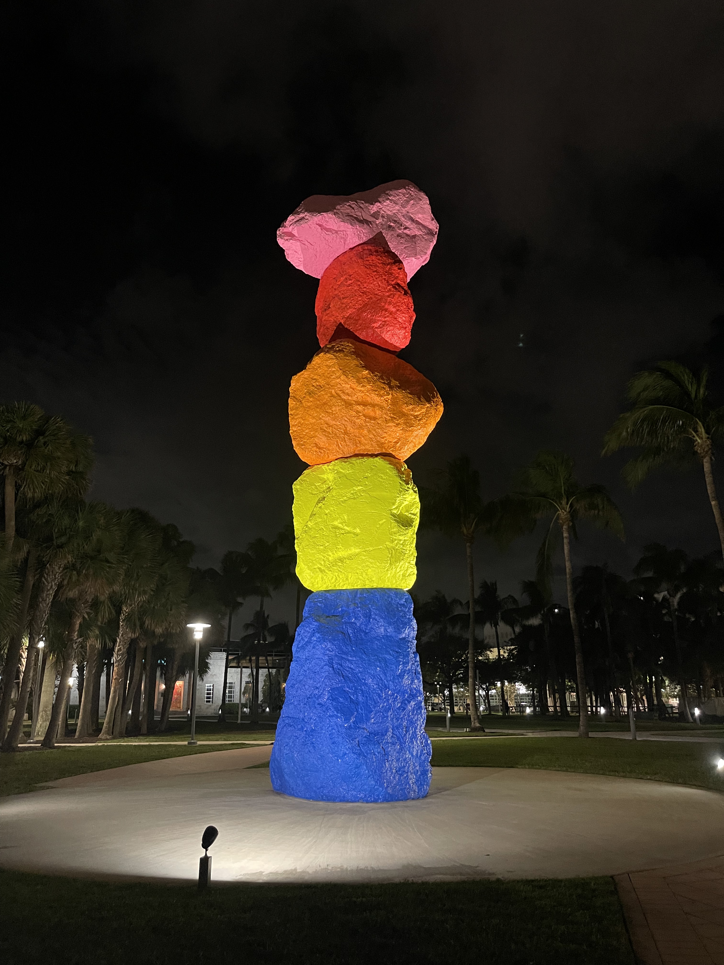 A tall sculpture of five neon-colored boulders stacked vertically, lit against a dark night sky.