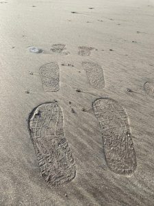 Sandy beach with two pairs of shoe prints fading into the distance.
