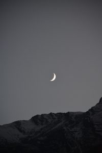 Crescent moon glowing above a snow-dusted mountain range at twilight.
