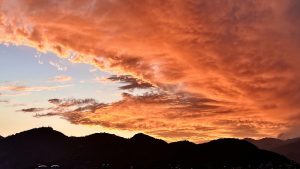 Dramatic fiery sunset sky blazing in deep orange and crimson above dark silhouetted mountain ridgelines 