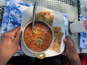 A rich, thick mutton karahi curry, garnished with fresh coriander, served in a traditional metal balti with two handles, alongside pieces of layered chapati flatbread. 