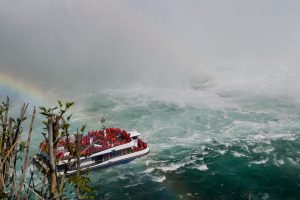 Red-poncho-clad tourists aboard a boat engulfed in thundering mist and turquoise churning waters beneath a rainbow 