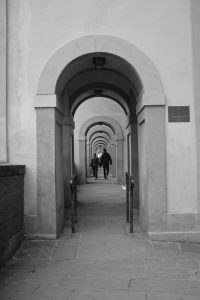 Black and white photo of two people walking through a row of colonnades in Florence, Italy.