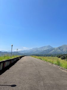 Straight pathway lined with lamp posts leading toward distant mountains beneath a clear blue sky. 
