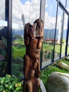 Weathered wooden totem carving against glass building, mountains and stone garden in background
