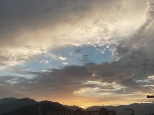 Dramatic sunset sky with golden clouds over silhouetted mountain hills and rooftops, Nepal 