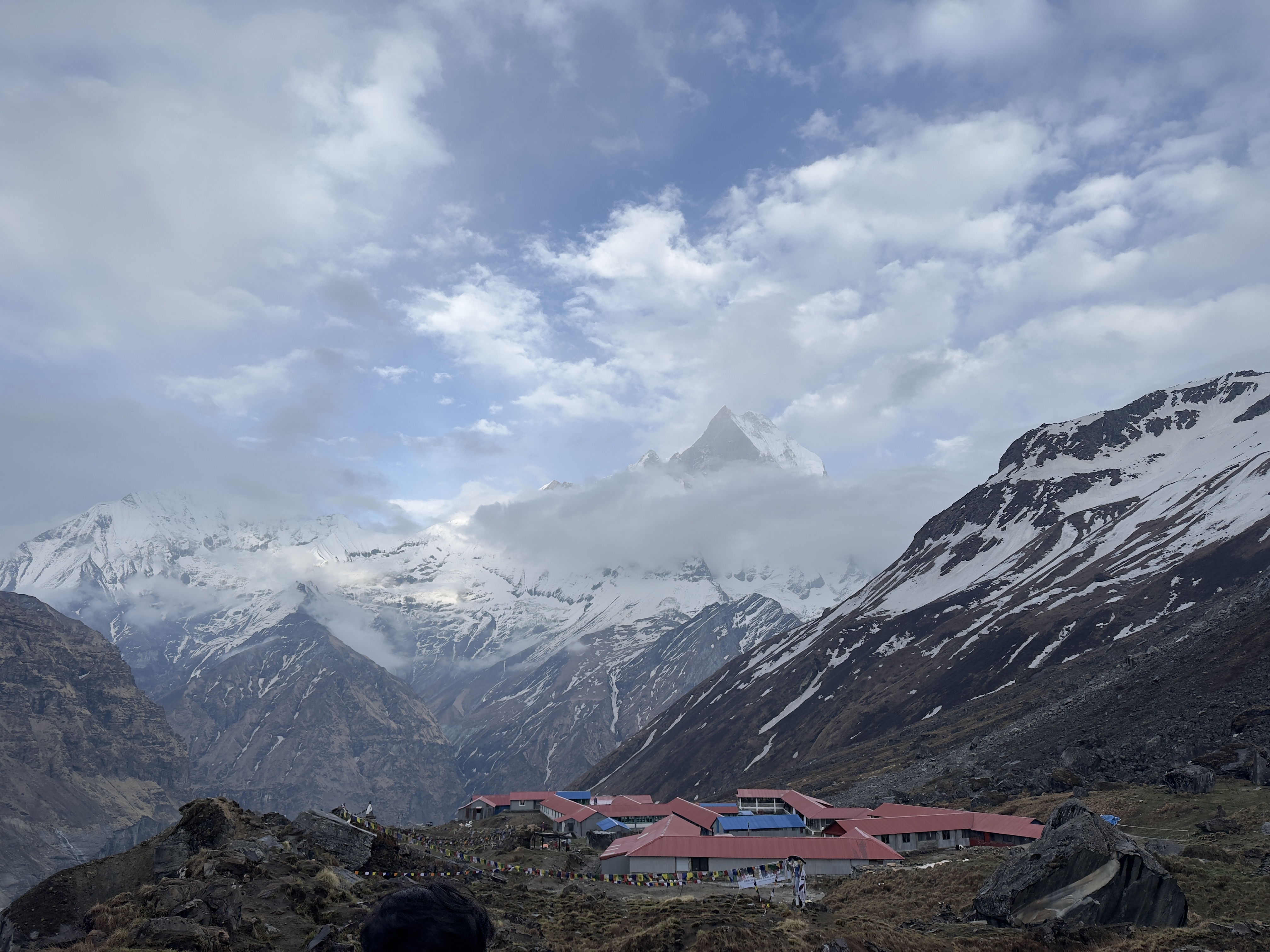 Snow-capped mountains rise above the clouds, with red-roofed buildings nestled in the rocky landscape below.