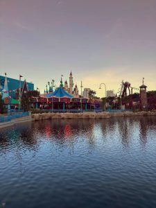 Colorful amusement park attractions and rides reflected in calm water during twilight. 