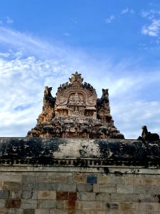 Ornate temple facade with intricate stone carvings, set against a bright blue sky with scattered clouds. 
