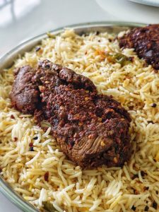 Close-up of a spiced, grilled meat piece on a bed of fluffy, white rice speckled with herbs and spices