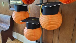 Decorative orange balls made of paper, about the size of a basketball, wearing graduation hats.