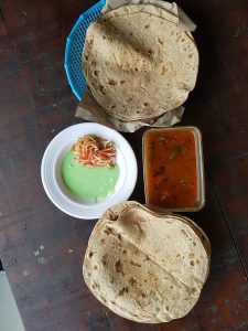 Top view of Pakistani kofta with raita, served with flatbreads, spicy curry, and a side of green sauce and salad on a dark wooden table.
