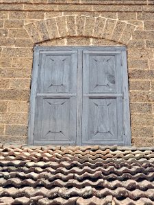 A traditional wooden window set in laterite stone walls overlooks rows of old clay roof tiles. The simple design reflects the timeless beauty of Kerala's heritage architecture. Captured at Varikkasseri Mana, Vaniyamkulam, Palakkad.
