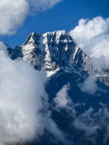 Snow-capped Sisne Himal (Murkutta Himal) in East Rukum, surrounded by fluffy white clouds beneath a bright blue sky, conveying grandeur and tranquility.