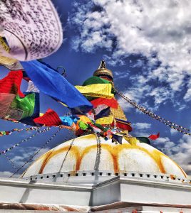 Buddhist stupa with colorful prayer flags flutters against a vibrant blue sky. White dome and ornate spire convey serenity and spirituality.