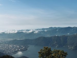 Aerial view of Pokhara city and Phewa Lake nestled among forested hills with low clouds, Nepal 