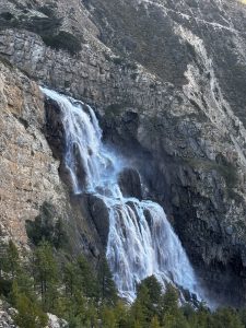 A majestic waterfall cascades down a rugged cliff surrounded by lush green trees.