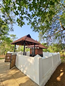 A traditional Kerala-style shrine stands peacefully beneath a large banyan tree inside the temple grounds. The tiled roof and white compound wall reflect Kerala's timeless temple architecture. Captured at Niramkaitha Kotta Bhagavathi Temple, Vallikunnu North, Malappuram.