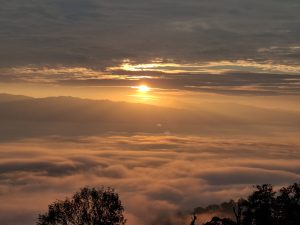Dramatic sunrise view above a blanket of clouds with golden light breaking through dark storm clouds.