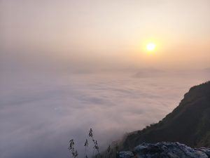 Sunrise over a misty mountain landscape, with soft clouds covering the valley.