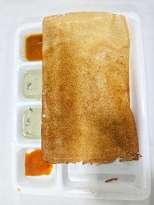 A crispy golden-brown dosa served on a white compartment tray with coconut chutney and red chutney on the side