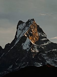 Close-up of Machhapuchhre with golden alpenglow on its rocky face against a moody sky 