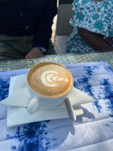 A white ceramic cup filled with a hot cappuccino beverage featuring detailed crescent-moon latte art on its foam surface.
