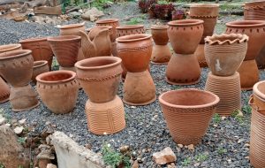 A large assortment of unglazed terracotta clay pots in various sizes, shapes, and carved linear patterns. 