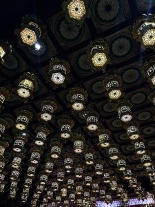 Rows of ornate hanging lanterns beneath a decorative patterned ceiling, creating a symmetrical display of light and design. 