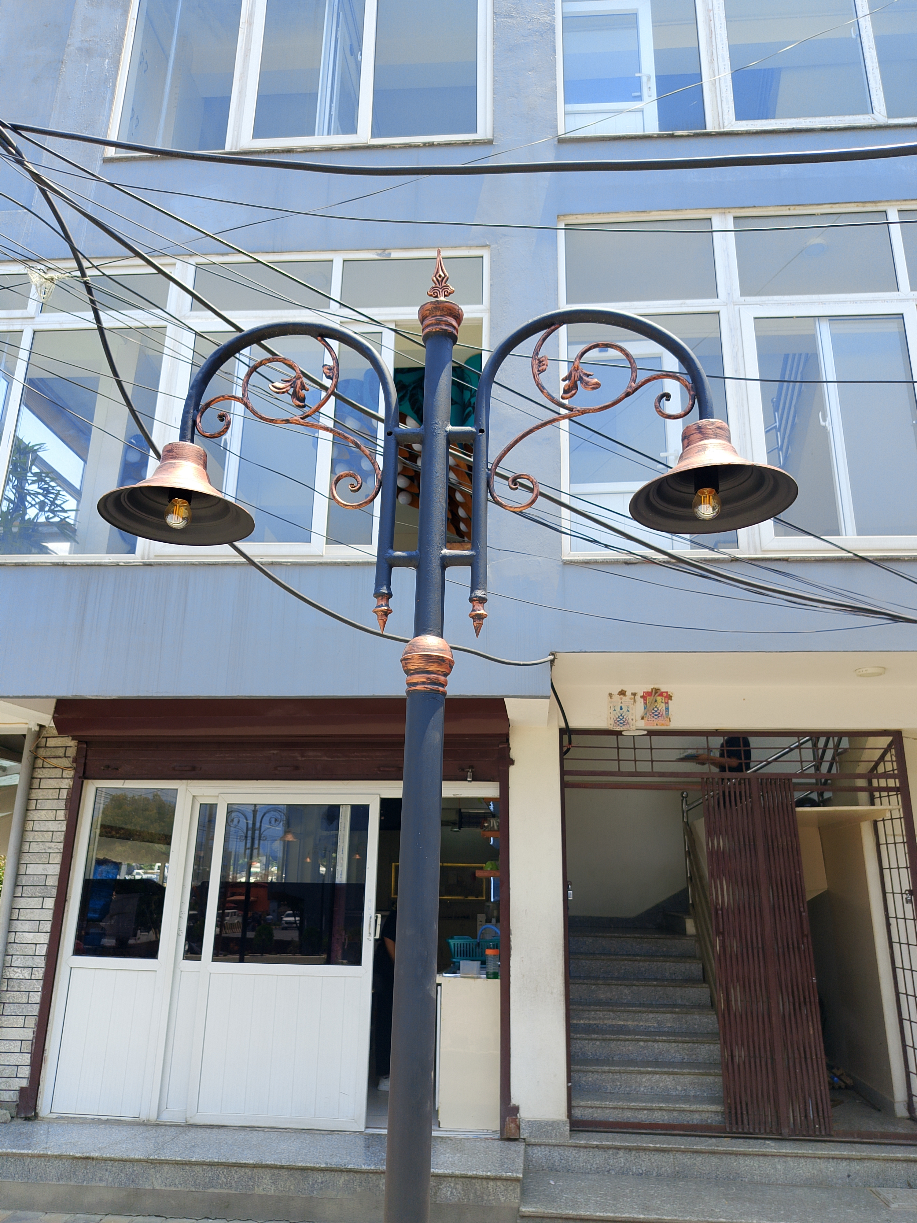 Decorative double-arm street lamp with copper accents in front of a commercial building