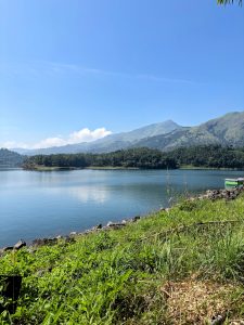 Peaceful mountain lake surrounded by forests and distant hills under a bright blue sky. 
