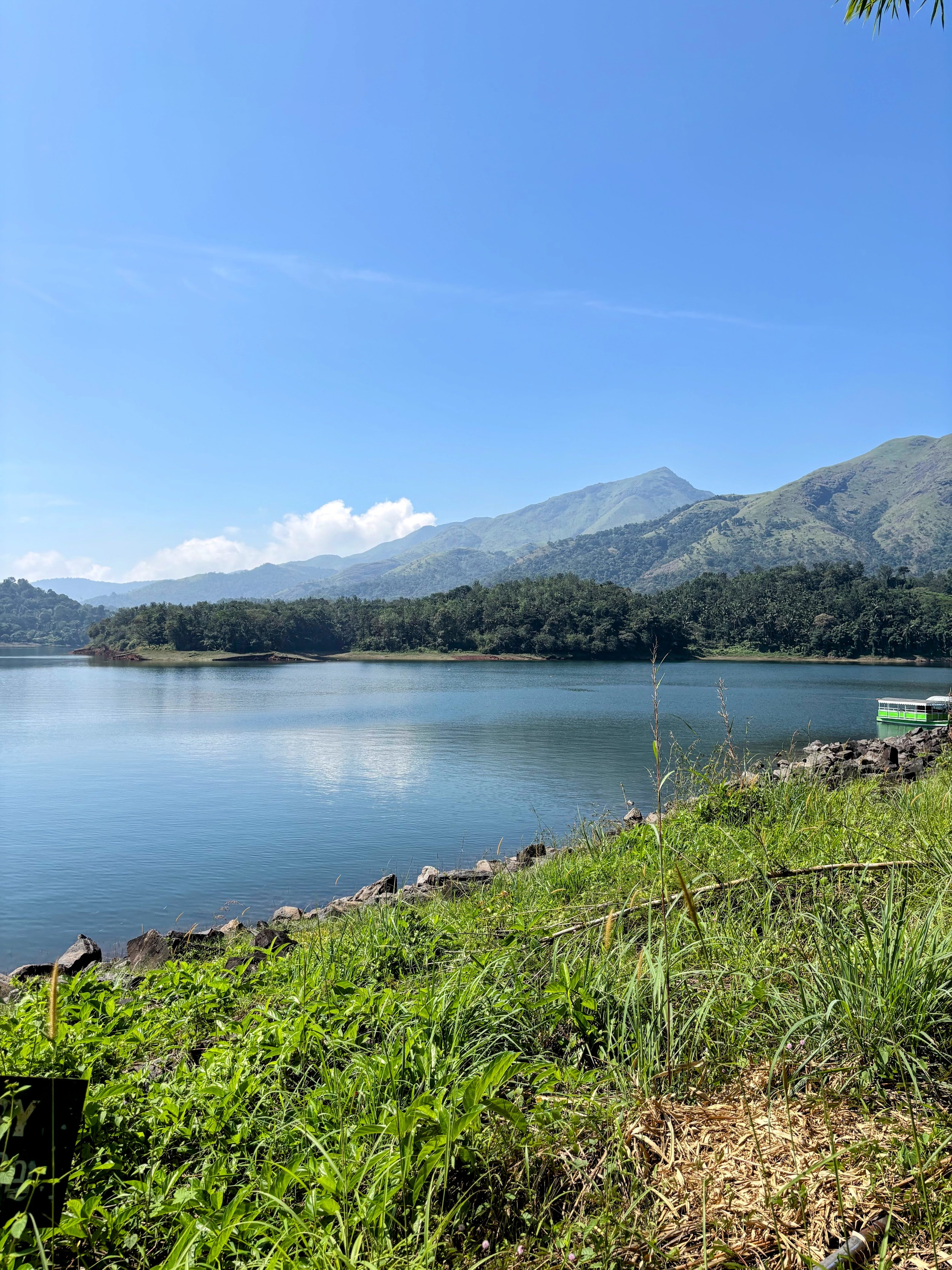 Peaceful mountain lake surrounded by forests and distant hills under a bright blue sky.