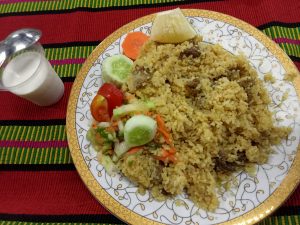 A plate full of Biryani and salad with a glass of curd 