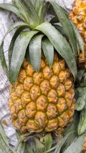 Ripe pineapple with golden-yellow textured skin and a fresh green leafy crown, resting on newspaper, highlighting its natural pattern, vibrant color, and tropical freshness.